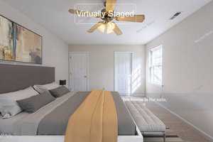 A virtually staged bedroom with a modern bed featuring gray and beige bedding, a ceiling fan, and neutral walls. A large window lets in natural light, and a contemporary painting hangs above the bed. Text reads "This home is for sale.