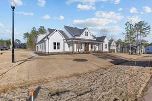 A modern, two-story suburban house with a white exterior and gray roof sits on a large, newly landscaped lawn. The sky is clear with a few clouds, and several trees are visible in the background.