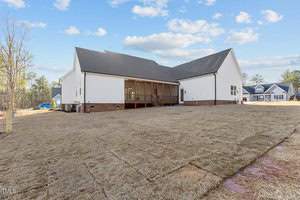 A large, modern white house with a black roof is seen from the backyard. It features a screened porch and is set on a newly sodded lawn. The sky is clear with a few clouds, and surrounding houses are visible in the distance.
