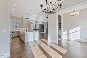 Spacious modern interior with an open-concept kitchen and living area. Features include large windows, hardwood floors, a central island, and contemporary chandeliers. Natural light fills the space, enhancing the minimalist design.