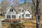 Nestled at 627 Enon Road, this charming white house in Oxford features a gabled roof, black shutters, and a brick foundation standing amidst a wooded area. A small staircase leads to the teal front door, while a curving path winds through the front yard. Trees partially shadow the scene.