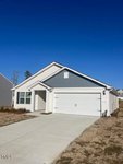 The single-story house at 110 Cultivar Street in Oxford boasts a gray and white exterior, featuring a two-car garage and a small front porch. The yard is mostly bare, with some young shrubs near the front. The sky is clear and blue.