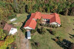 The aerial view showcases a large house with a red roof at 2701 Propus Wilkinson Road, surrounded by green trees. The property includes a small white building to the left and a tent-like structure adjacent to the main house. A grassy yard completes this serene Bullock setting.