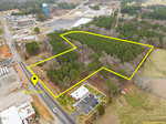 Aerial view of a wooded area outlined in yellow, adjacent to 729 Lewis Street in Oxford. Nearby are commercial buildings, roads, and a water tower. The surrounding landscape includes trees and open land.