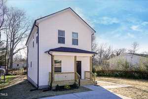 The charming two-story white house at 223 W College Street features a small porch, dark roof, and wooden stairs leading to the front door. Surrounded by a grassy yard and trees under Oxford's clear blue sky, it promises serene living.