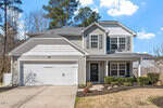 Nestled at 730 Forrest Lane, this two-story gray house with white trim offers a charming glimpse of Creedmoor. Featuring a double garage and a cozy front porch, its well-maintained landscaping includes lush shrubs and a grassy yard, framed by tall trees under a partly cloudy blue sky.