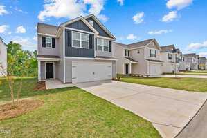 In the suburban neighborhood along 106 Anaheim Street, a row of modern two-story houses features two-car garages and neatly trimmed lawns under an Oxford-blue sky dotted with a few clouds.