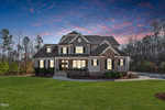 Suburban two-story house at 3705 Dillard Lane with a gabled roof and stone facade, warmly lit windows against a twilight sky. Nestled in serene Wake Forest, it is surrounded by manicured lawns and trees, creating an inviting atmosphere.