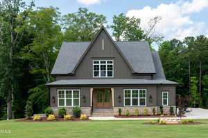 Located at 3985 Hope Valley Drive in Wake Forest, this charming two-story house with dark gray siding and a sloped roof is surrounded by lush green trees. The front yard boasts a well-kept lawn and small shrubs near the entrance, all under a clear blue sky.