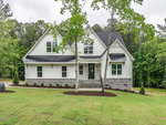 Nestled at 3402 River Manor Court in Franklinton, this modern two-story house boasts a white facade, dark roof, and stone accents. Set amid a grassy yard and surrounded by trees, the home features large windows and a small front porch with two steps leading to the entrance.