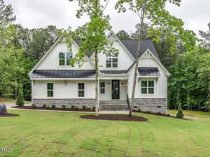 Nestled at 3402 River Manor Court in Franklinton, this modern two-story house boasts a white facade, dark roof, and stone accents. Set amid a grassy yard and surrounded by trees, the home features large windows and a small front porch with two steps leading to the entrance.