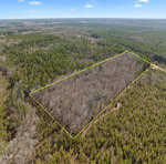 Aerial view of a rectangular forested area, outlined in yellow near 1557 Satterwhite Road, Oxford. Surrounded by dense green trees, the outlined section has fewer trees, creating a stark contrast in vegetation density. The sky remains clear with just a few clouds floating by.