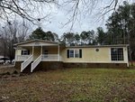 Nestled at 4004 Hurst Drive in Franklinton, this single-story yellow house features a cozy covered porch with white railings, set against a grassy lawn. Large windows grace the home perched on its brick foundation, surrounded by bare trees under a cloudy sky.