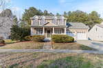 Front view of a two-story suburban house at 203 Oxford Park Boulevard, featuring a gray exterior with a covered porch and two columns. This Oxford residence includes a two-car garage, paved driveway, and small front yard adorned with bushes and trees under a clear blue sky.