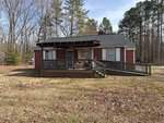 A small, red-brick house on 8658 US-15 with white trim and an accessible ramp leads to a covered front porch. It's surrounded by bare trees and evergreens in Bullock, set in a grassy yard with scattered fallen leaves under a partly cloudy sky.