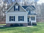 Nestled on 3692 Summer Springs Drive in Franklinton, this two-story house features beige siding, blue shutters, and white trim. Its gabled roof overlooks a small front porch with steps, bordered by a grassy yard and a wooded backdrop under a partly cloudy sky.