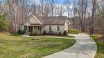 Nestled in the woods at 4334 N Greg Allen Way, Oxford, this single-story house boasts a gabled roof. A curved driveway leads to a two-car garage, surrounded by a well-maintained lawn and mature trees. The sky above is partly cloudy.