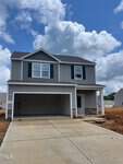 Located at 106 Scoville Street in Oxford, this newly constructed two-story house boasts gray siding and a dark gray roof. It features white trim, black shutters, and a stone accent on the lower facade. A double garage sits in front, and the freshly paved driveway complements the partly cloudy sky.
