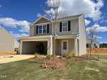 Nestled on 104 Anaheim Street, this two-story beige house in Oxford boasts a two-car garage and a quaint front yard. The open garage door reveals an empty space. Above, the sky is clear with a few fluffy clouds, while young trees and bushes adorn the landscape.