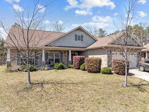 A charming single-story brick house on 1162 Phelps Court features a gabled roof and is surrounded by a front yard with leafless trees and bushes. The partly cloudy skies add to the serene atmosphere. A driveway, perfect for easy access, is visible on the right side.