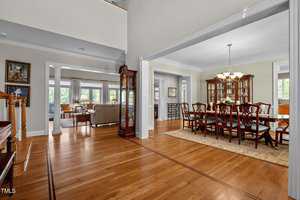 Spacious interior with a formal dining area featuring a wooden dining table and chairs, chandelier, and china cabinet. Adjoining room has a sitting area with sofas. Hardwood floors and large windows provide a warm, inviting atmosphere.