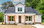 Located at 205 Rogers Avenue in Creedmoor, this white, modern farmhouse-style home boasts a striking black roof and a welcoming front porch with wooden columns. Large windows and a brown wooden front door are complemented by a newly planted garden and fresh landscaping.