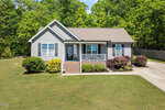 Nestled at 424 Angus Place, this quaint single-story house with gray siding and a brown roof features a small front porch with white railings. Surrounded by a well-maintained lawn, the charming landscape includes shrubs and trees under a clear blue sky.