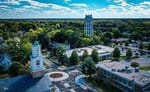 Aerial view of a small town near Oxford, showcasing a church with a green dome, a water tower, and several buildings enveloped in lush greenery under a blue sky with scattered clouds. A roundabout graces the main road by 404 Broad Street.