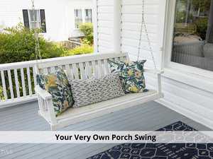 A white porch swing with floral and patterned cushions hangs on a porch. Below it is a dark blue patterned rug. The caption reads, "Your Very Own Porch Swing." A white house and greenery are in the background.
