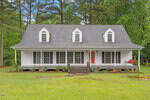 Located at 2011 Evans Road in Franklinton, this charming white two-story house boasts a gabled roof and dormer windows, highlighted by a vibrant red front door. A wide front porch with a red swing invites relaxation, while lush greenery and tall trees frame the well-maintained lawn.
