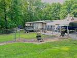 Nestled at 3104 Piney Point Road, this single-story mobile home is surrounded by a lush canopy of trees. A chain-link fence and satellite dish complement the setting, while a covered carport holds a boat. Potted plants line the yard's edge, adding charm to this Bullock retreat.