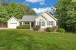 Nestled at 4047 Brooksdale Drive, this charming Franklinton single-story house boasts light beige siding, a gabled roof, and an attached garage. The front yard features well-maintained shrubs and a grassy lawn, surrounded by tall, lush trees under a blue sky with scattered clouds.