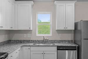 Modern kitchen with white cabinets, granite countertops, stainless steel dishwasher, and refrigerator. A window above the sink lets in natural light, offering a view of greenery outside.