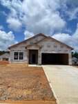 A single-story house is under construction at 109 Scoville Street in Oxford, draped in protective wrap adorned with brand logos. It rests on a bare, reddish dirt lot with a newly paved driveway, set against a backdrop of partly cloudy skies.