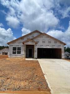 A single-story house is under construction at 109 Scoville Street in Oxford, draped in protective wrap adorned with brand logos. It rests on a bare, reddish dirt lot with a newly paved driveway, set against a backdrop of partly cloudy skies.