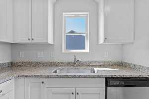 A modern kitchen with white cabinets, granite countertops, and a stainless steel sink. A window above the sink reveals a view of a neighboring house. The kitchen includes a stainless steel dishwasher on the right.