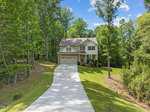 Nestled in the serene surroundings of 1321 Sourwood Drive, this two-story house features a beige exterior with charming red shutters. Located in Wake Forest, it boasts a long, winding driveway leading to an attached two-car garage, all embraced by well-maintained, lush green lawns and towering trees.