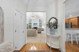Bright living room entrance with hardwood floors, a small table with a plant, and a large decorative mirror on the right. Arched doorway reveals a cozy sitting area with a chandelier, sofa, and a TV on the back wall. Image source: TMLS.