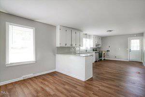 Spacious kitchen with wood flooring, white cabinets, and a tile backsplash. Features include a kitchen island with a breakfast bar, stainless steel appliances, and a window for natural light. An open floor plan with a door leading outside.