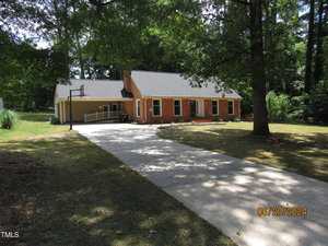 A single-story brick house with a shingled roof is partially shaded by large trees. The house features a basketball hoop beside the driveway. The lawn is mostly green, and the driveway leads to the front entrance. Date stamp reads 06/20/2024.