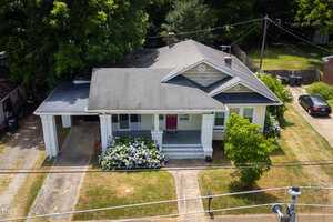 Aerial view of the single-story white house at 422 Hancock Street, Oxford, featuring a dark roof, front porch, and carport. The yard is flanked by flowering bushes and trees in the back. A gray car sits in the driveway, with a sidewalk and power lines running along the front.