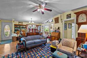 A cozy living room with a blue couch, patterned rug, and various antique furniture. On the left, there's a wooden cabinet and a globe. A ceiling fan hangs above, and natural light fills the room through windows and an open door.