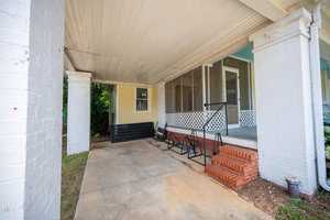 Covered porch area with concrete flooring and brick steps leading to a screened door. The porch is framed with white columns, and a yellow siding exterior wall is visible. A lattice design is featured beneath the screens.