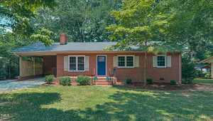Nestled at 208 Hillcrest Drive in Oxford, this charming red-brick house with a blue front door and covered carport boasts a well-maintained lawn, surrounded by tall trees that offer ample shade and a serene atmosphere.