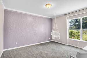 A room with a purple accent wall featuring a subtle wavy pattern. A white hanging chair is suspended near a large window, which offers a view of greenery outside. The room has light gray carpet and a ceiling light fixture.