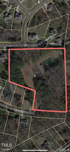 Aerial view of a wooded area with a red outline, surrounded by residential streets labeled Bluegrass Dr and Robin Rd. The image shows nearby houses, open spaces, and dense trees.