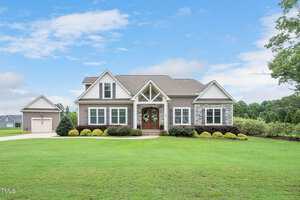 A suburban house on 4555 Austins Lane in Franklinton features a well-maintained lawn, gray siding, and stone accents. It boasts a gabled roof and a welcoming porch with a brown double door. A two-car garage sits to the left, framed by trees and a partly cloudy sky.