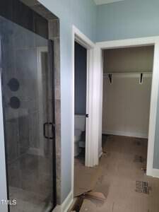 A bathroom with a modern glass shower on the left and a toilet in a separate small room straight ahead. The floor is covered with protective cardboard, suggesting ongoing construction or renovation.