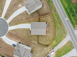 Aerial view of a cul-de-sac with three houses. The central house has a fenced backyard. A road runs alongside the properties. The area appears to be newly developed with minimal landscaping.