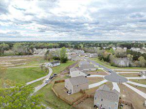 Aerial view of a suburban neighborhood with houses, winding roads, and green spaces. The sky is partly cloudy, and trees surround the area, creating a peaceful, residential atmosphere.